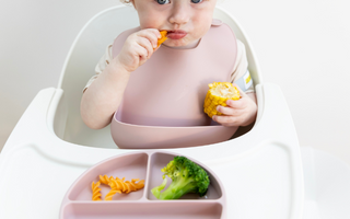 Baby eating corn and pasta with mess-free silicone bib and divided plate, easy clean, food-safe design