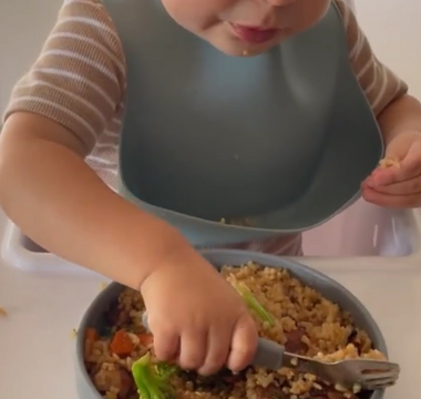 Toddler eating rice and veggies with bib, mess-free mealtime solution
