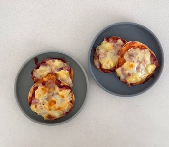 Two gray plates with mini cheesy pizzas on a clean countertop, perfect for mess-free meals.