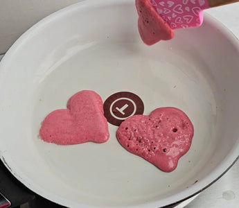 Pink heart-shaped pancakes cooking in white pan with spatula, perfect for mess-free family meals