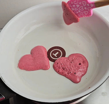 Pink heart-shaped pancakes cooking in white pan with spatula, perfect for mess-free family meals