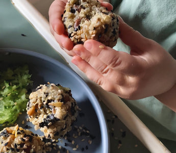 Child's hands holding sesame-coated rice ball over plate, mealtime mess-free with catch tray