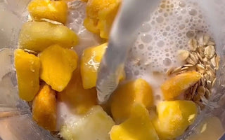 Milk pouring into blender with frozen mango chunks and oats for smoothie prep