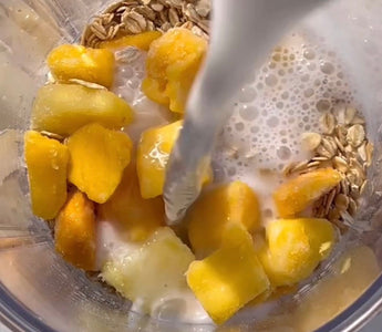 Milk pouring into blender with frozen mango chunks and oats for smoothie prep