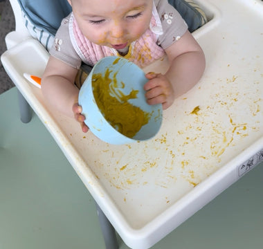 Baby eating messy puree in high chair with food-safe catch mat, easy wipe clean, protects floors