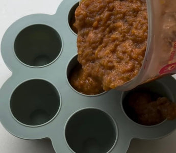Pouring baby food puree into silicone storage cups for easy meal prep and freezing.